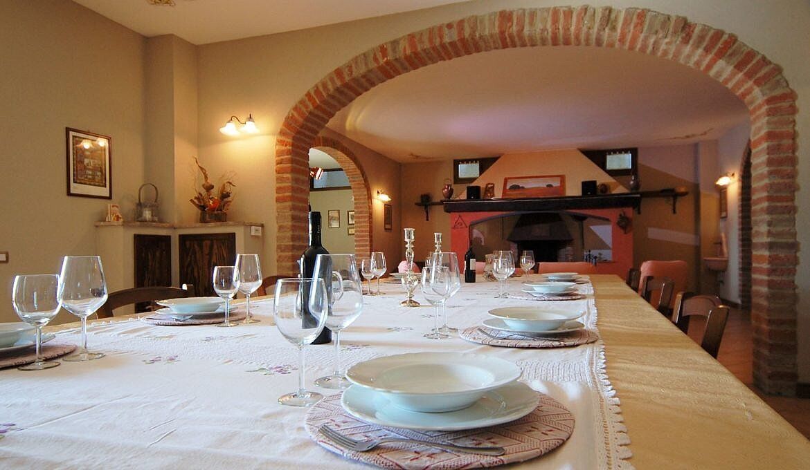 Un espace repas avec une longue table dressée pour un repas, agrémenté d’une arche en briques, d’une cheminée et d’un téléviseur fixé au mur.