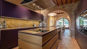 A modern kitchen with a central island, purple cabinets, and a stone archway leading to an outdoor area.