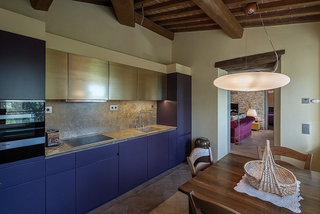 Una cucina moderna con mobili blu scuro, zoccolo in pietra e tavolo da pranzo in legno con cesto intrecciato.