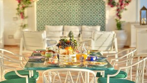 A dining table set with plates, glasses, and a pitcher of orange juice, surrounded by white chairs with green cushions. - Villa Atena: A charming two-story villa which faces the sun and the sea, with Free WI-FI. (Praiano)