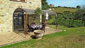A stone building with a patio area featuring a table and chairs, a covered seating area, and a large planter. - Villa Campanella: A characteristic and welcoming two-story age-old farm house surrounded by the greenery, with Free WI-FI. (Perugia)