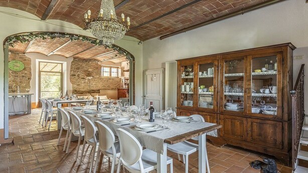 A dining area with a long table set for a meal, a wooden cabinet with glass doors, and a stone wall in the background. - Villa Pernice: An elegant and welcoming two-story villa surrounded by the greenery, with Free WI-FI. (Castiglione D'orcia)