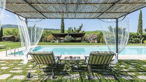 A pool area with two chairs and a table under a pergola with a view of the pool and surrounding landscape. - Villa Pernice: An elegant and welcoming two-story villa surrounded by the greenery, with Free WI-FI. (Castiglione D'orcia)