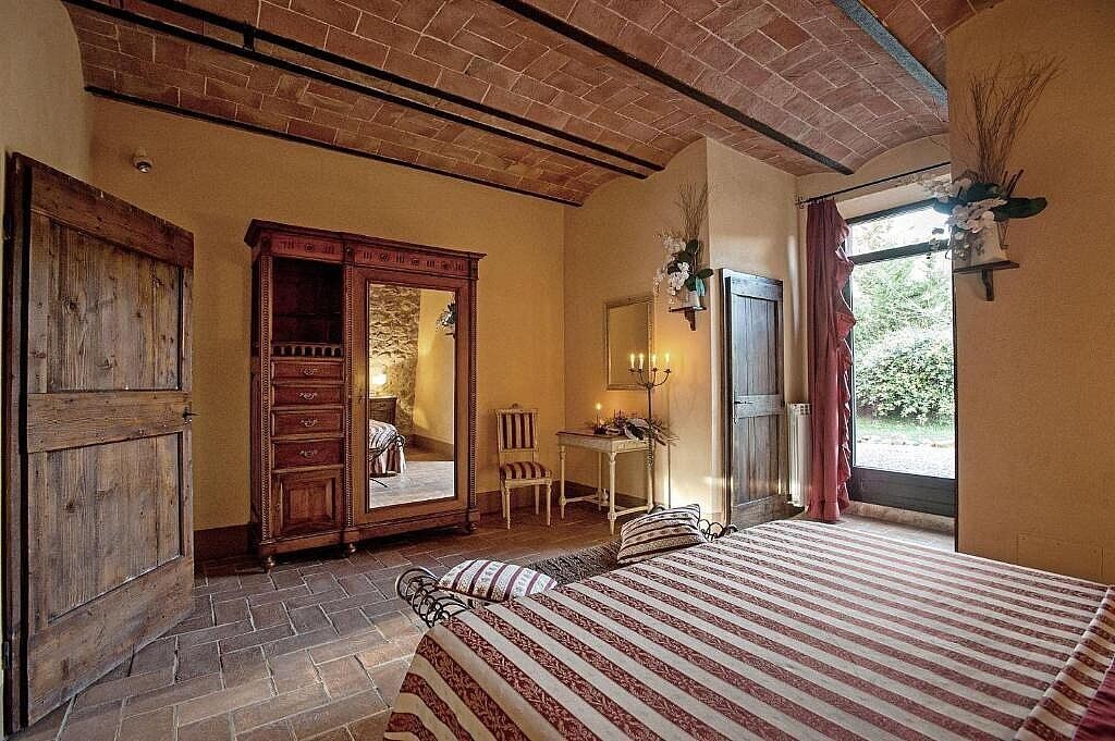 A bedroom with a bed, a wooden wardrobe, a desk with a chair, and a mirror.