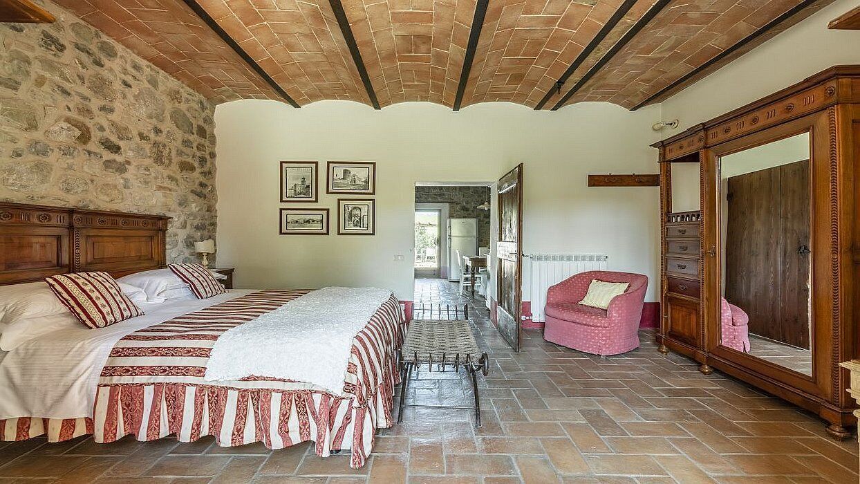 Een slaapkamer met een groot bed, een houten garderobe, een stenen muur en een betegelde vloer.