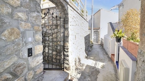 A narrow stone pathway leading to a gated entrance, flanked by white walls and a metal gate.
