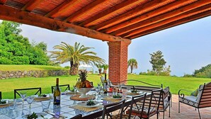 Un espace extérieur aménagé pour les repas, avec un pilier en briques, une table en verre et des chaises.