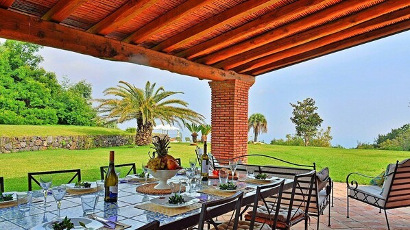 An outdoor dining area with a brick pillar, glass table, and chairs.