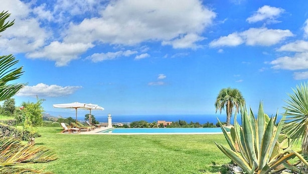 Un espace aménagé au bord de la piscine, avec vue sur l’océan, un parasol blanc et quelques chaises longues.