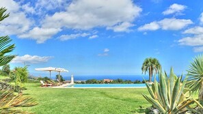 Zona junto a la piscina con vista al océano, una sombrilla blanca y algunas sillas de descanso.