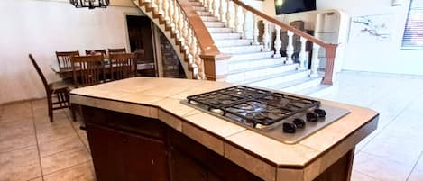 A spacious kitchen with a large island, wooden cabinets, and a staircase leading to an upper level.