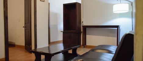 A room with a wooden bench, a black leather sofa, a wooden cabinet, and a wall-mounted lamp.