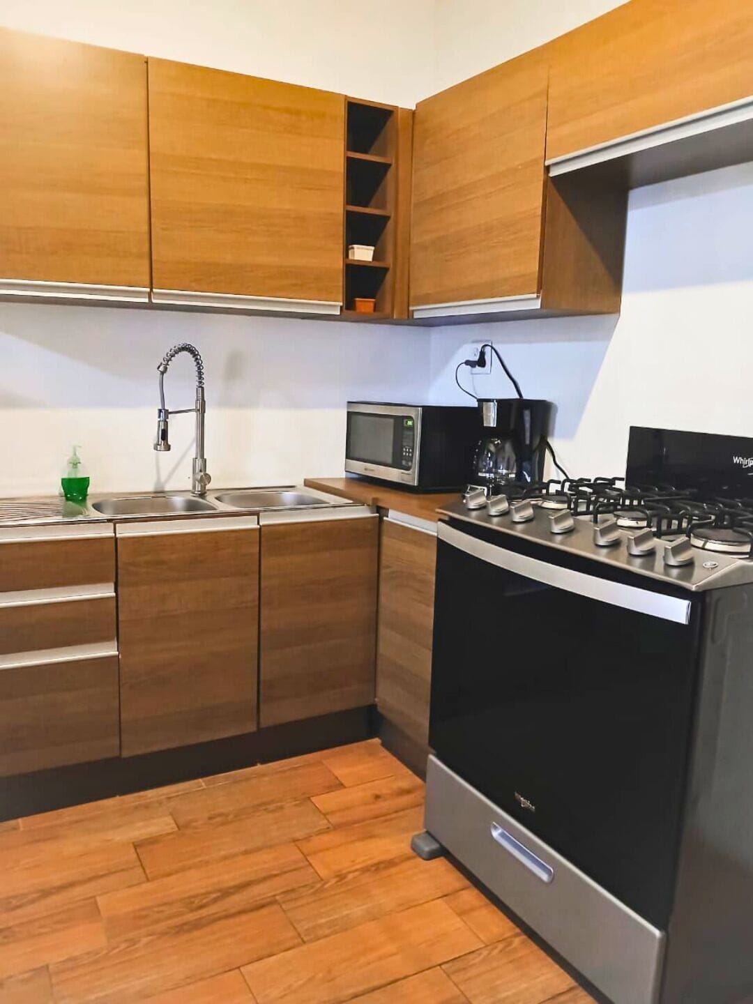 Una cocina moderna con armarios de madera, un lavamanos de acero inoxidable, microondas, cafetera y estufa a gas.