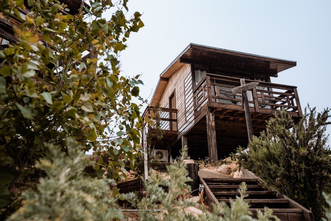 A wooden cabin with a balcony, surrounded by trees and shrubs.