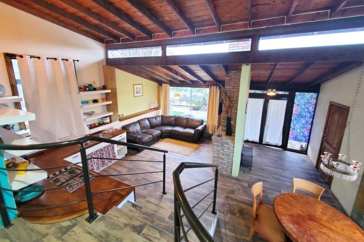 Un vaste espace de vie doté d’un plafond en bois, d’un canapé en cuir, d’une table à manger et d’un escalier menant à un autre niveau.