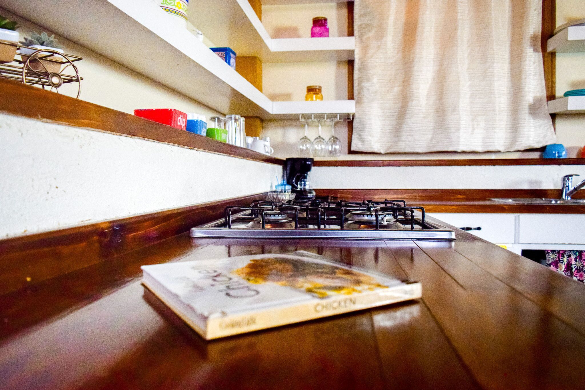 A kitchen with a gas stove, a cookbook, and various kitchen items on shelves.