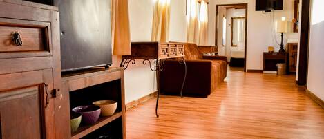 Amplia sala de estar con piso de madera, un sofá, un televisor y un mueble con cuencos.