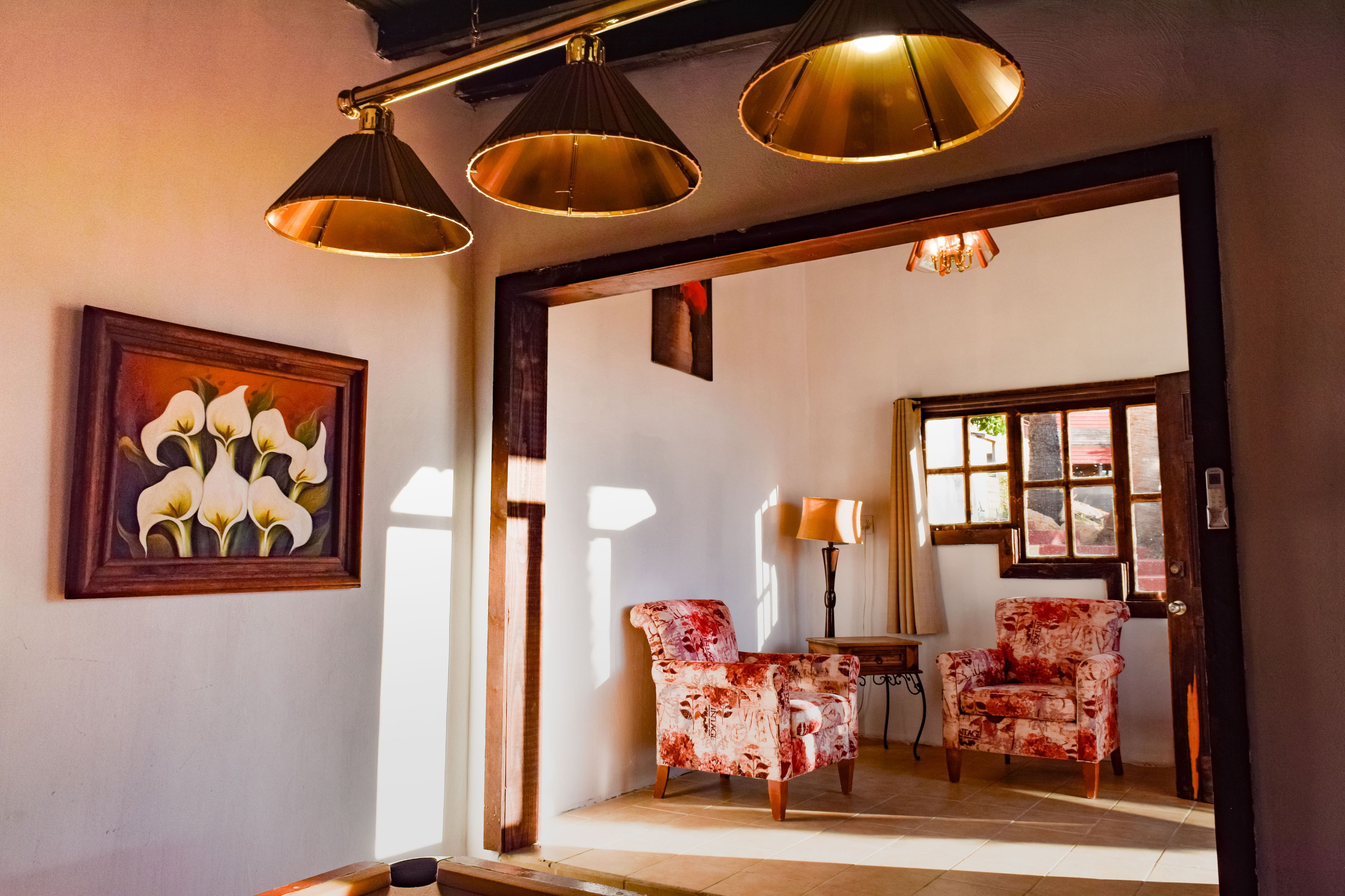 A room with a wooden door, a framed floral painting, two patterned armchairs, and a table.