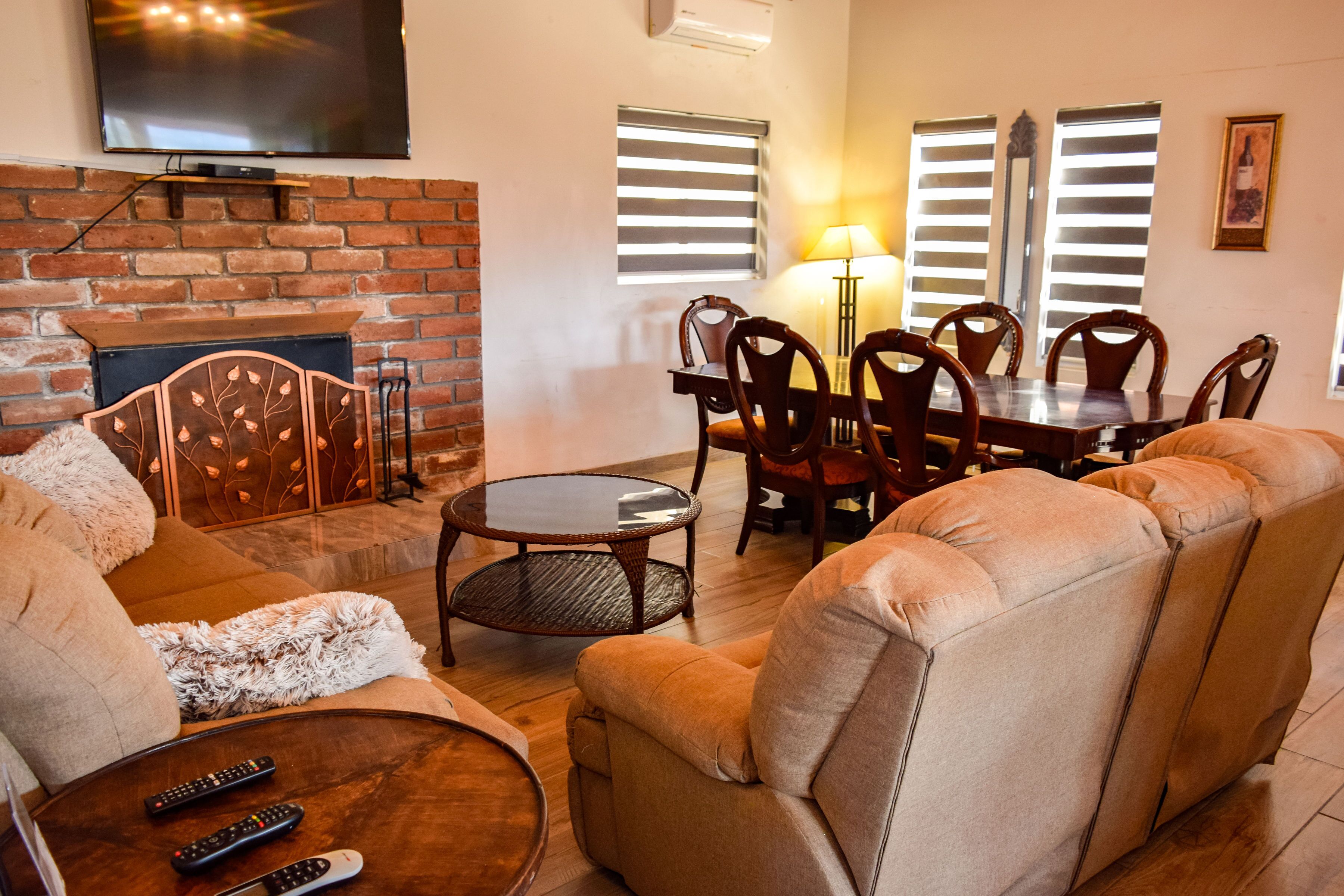 Una sala de estar con chimenea, televisor montado en la pared, mesa de comedor con sillas y sofá.