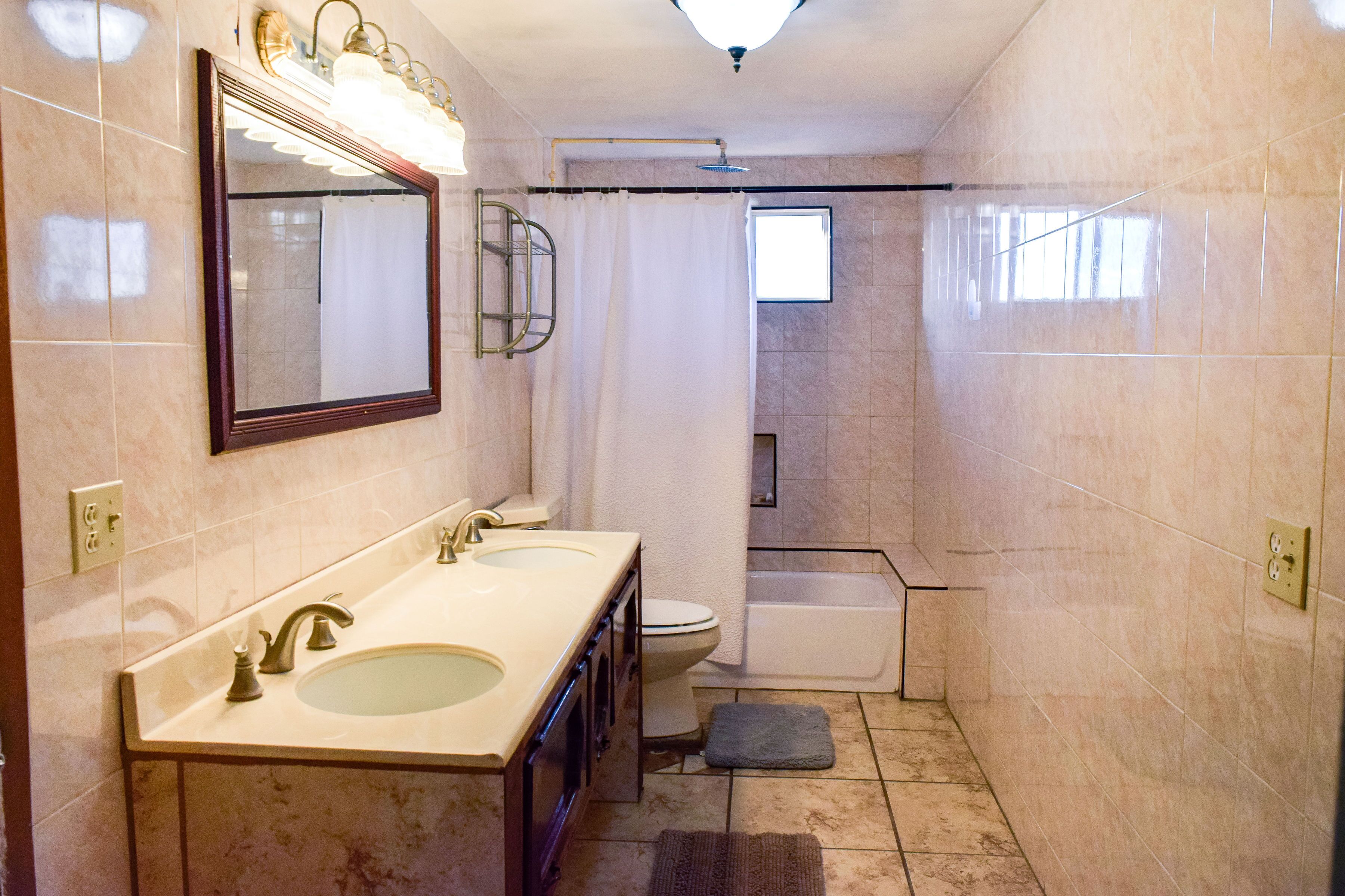 A bathroom with a double sink, a toilet, a shower, and a mirror.