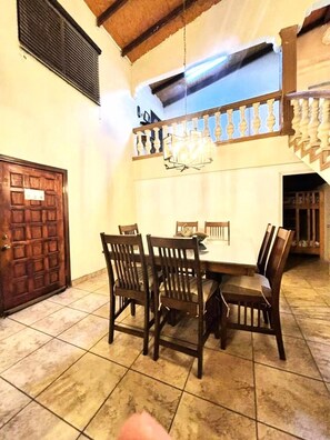 Un comedor con mesa y sillas de madera, un candelabro y un balcón con barandilla.