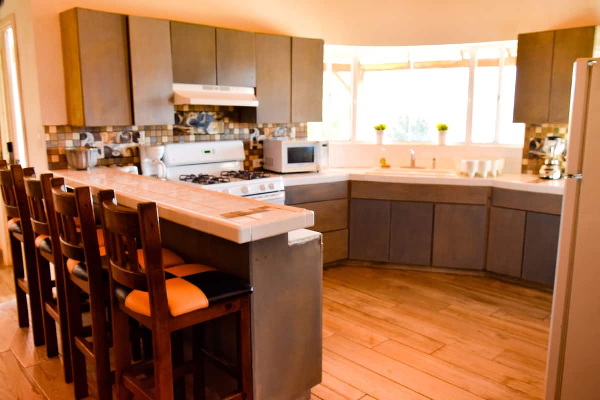 Une cuisine moderne dotée d’un îlot central, de chaises en bois, d’une cuisinière, d’un four à micro-ondes et d’un évier.