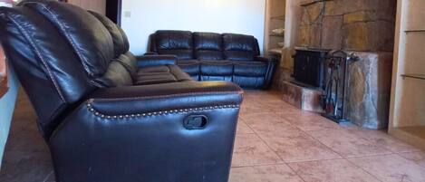 A spacious living area with a black leather sofa, a stone fireplace, and a staircase with a white balustrade.