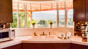 A kitchen with a large window, a sink, a microwave, and a blender.