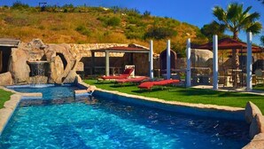 A swimming pool with a waterfall feature, surrounded by a stone border and green grass.