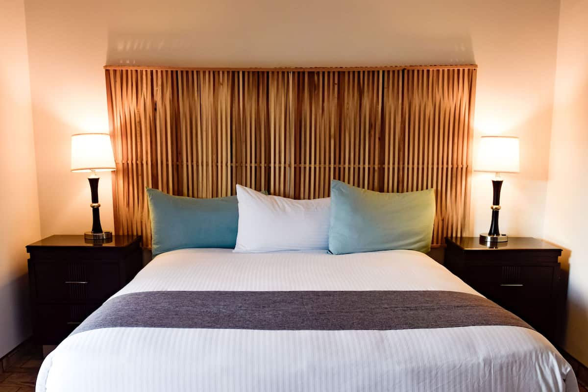 Une chambre d’hôtel avec un grand lit, deux tables de chevet avec des lampes et une tête de lit en bois.
