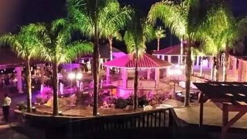 A nighttime outdoor area with palm trees, a covered seating area, and a pool.
