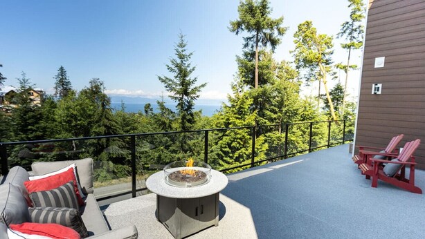 A balcony with outdoor seating, a fire pit, and a view of the forest and mountains.