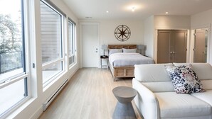 A bedroom with a large window, a bed with a wooden headboard, a white sofa, and a wall-mounted compass decoration.