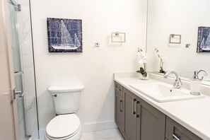 A modern bathroom with a toilet, a sink, and a shower. There are two framed artworks on the wall. - Executive Studio with Ocean & Mountain Views (Nanaimo)