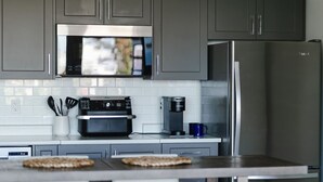 A modern kitchen with grey cabinets, a stainless steel refrigerator, a microwave, an oven, and a coffee maker.