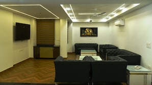 A modern living room with a sectional sofa, a flat-screen TV mounted on the wall, and a ceiling fan. - Pacific Inn Sec. 46 (Gurugram)