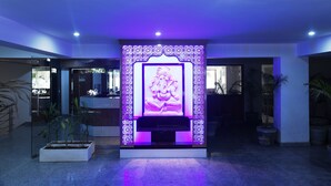 A reception area with a decorative wall featuring a central emblem, potted plants, and a modern design. - Pacific Inn Sec. 46 (Gurugram)