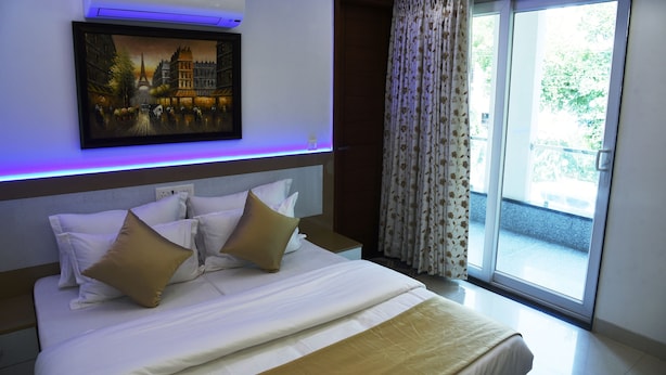 A hotel room with a bed, a painting, a window with curtains, and a view of the outside. - Pacific Inn Sec. 46 (Gurugram)