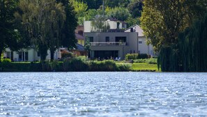 A lakeside property with a modern house, a balcony, and lush greenery. - House on the Havelbogen directly on the water with canoe and jetty, terrace apartment***** (Werder (Havel))