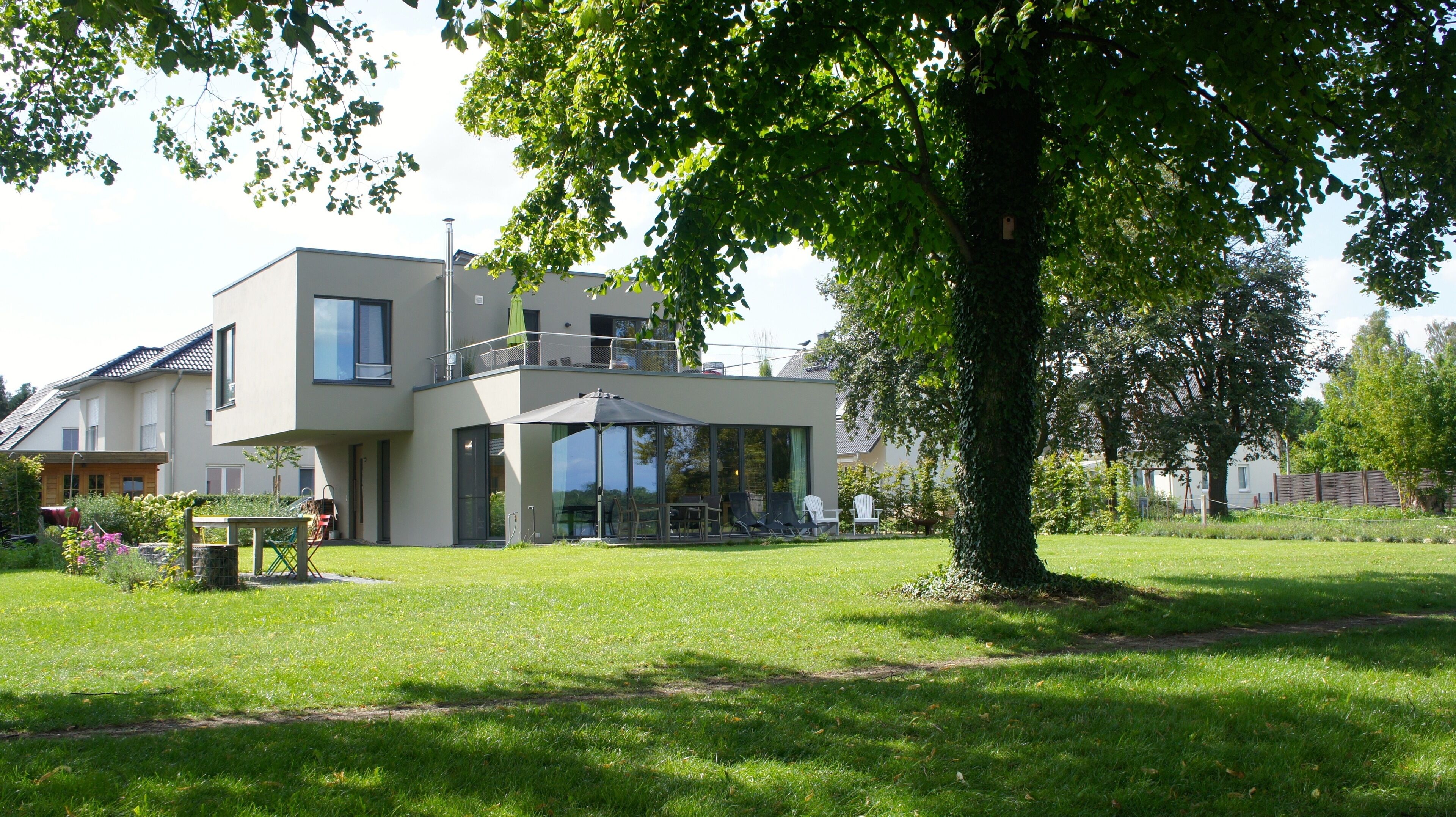 A modern two-story house with a balcony, large windows, and a well-maintained lawn.