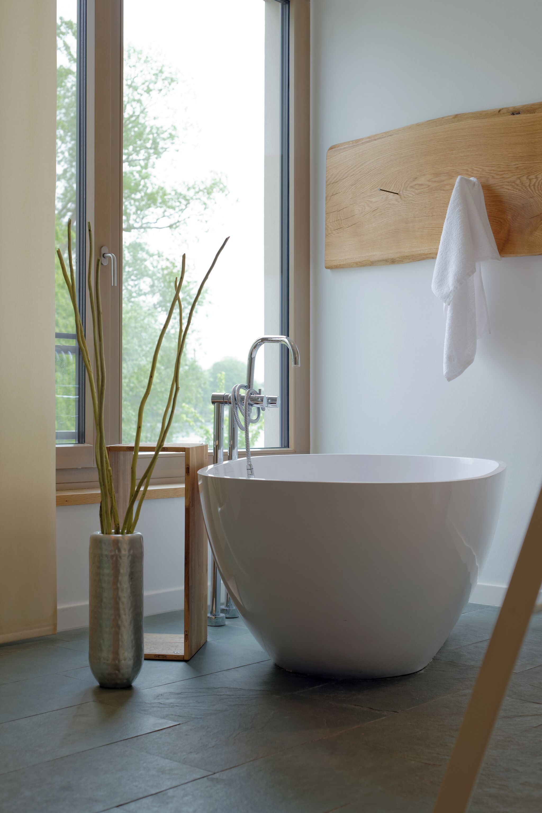 Un bagno moderno con una vasca freestanding, una testiera in legno e una finestra vista alberi.