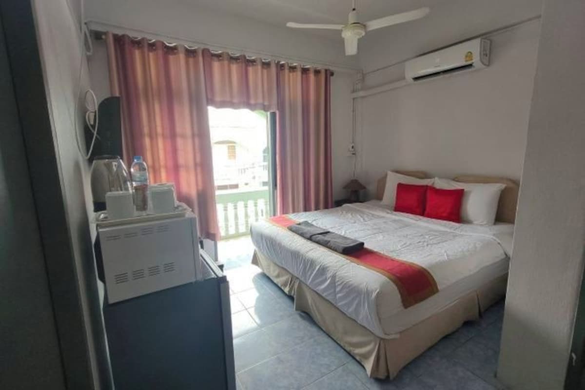 A hotel room with a bed, a desk with a computer, a ceiling fan, and an air conditioning unit.