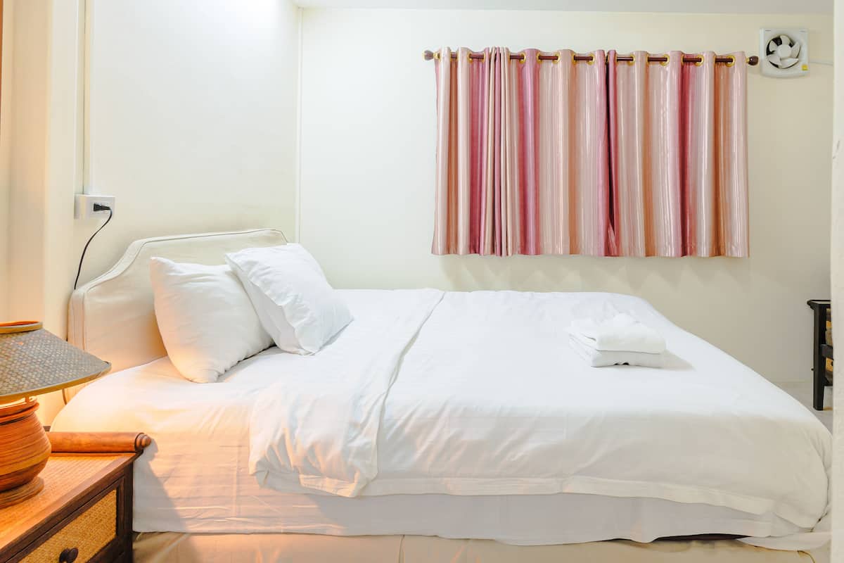 A neatly made bed with white bedding, a bedside table with a lamp, and a wall-mounted air conditioning unit.