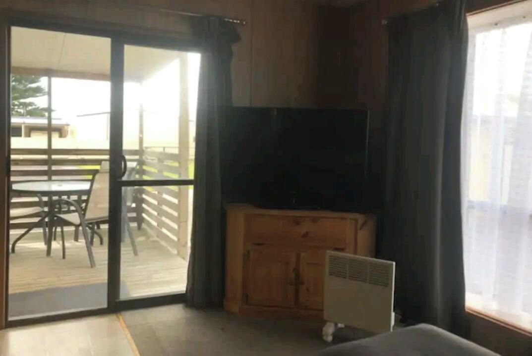 A room with a sliding glass door leading to an outdoor patio, a wooden cabinet, and a television.