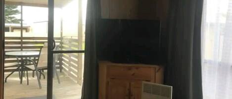 Une pièce dotée d’une porte-fenêtre coulissante donnant sur un patio extérieur, d’un meuble en bois et d’un téléviseur.