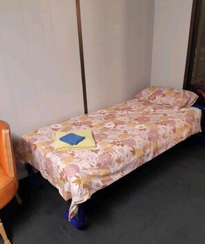 A single bed with a floral bedspread, a blue pillow, and a yellow item on the bed.