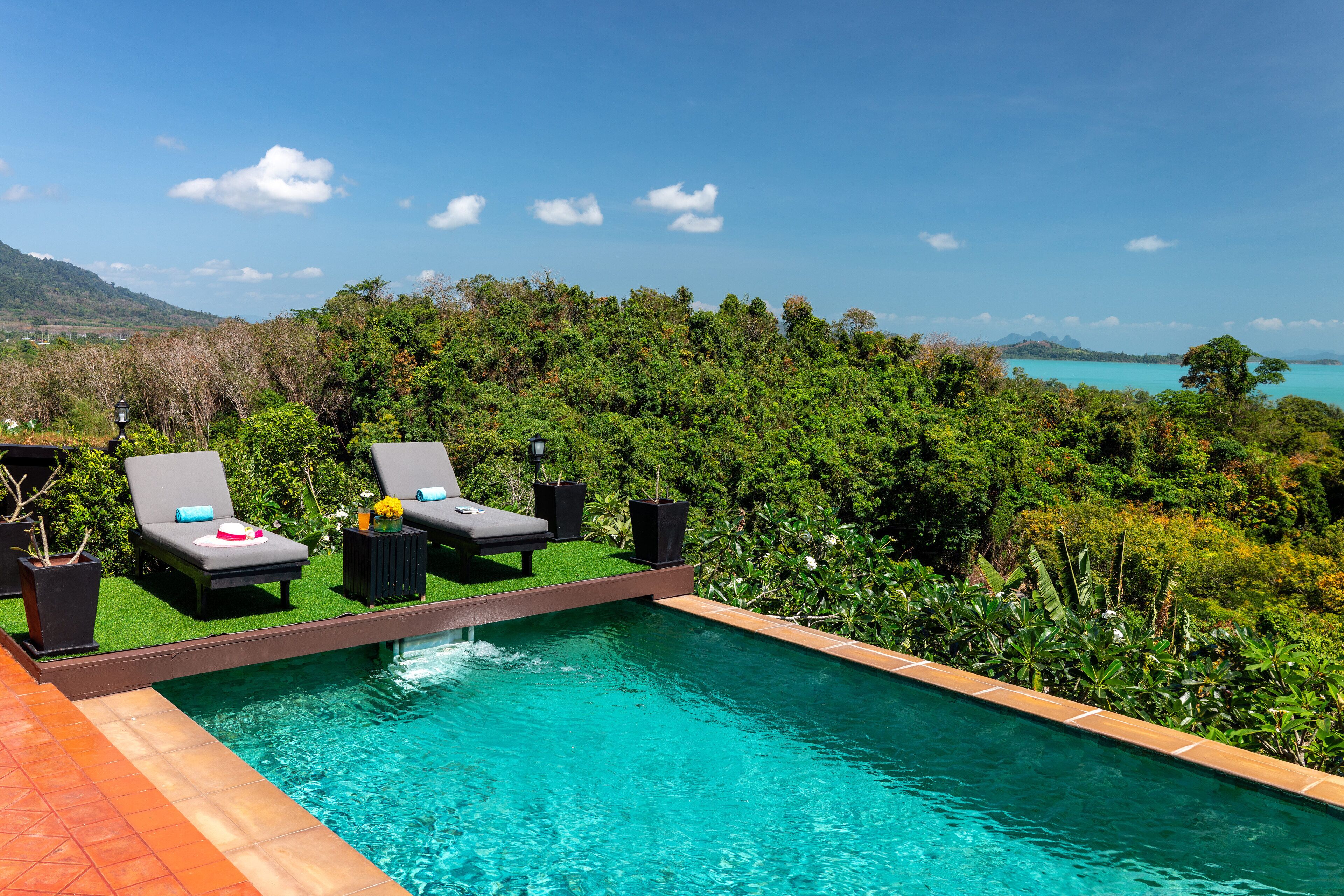 A swimming pool with lounge chairs and a view of a lush landscape and a body of water.