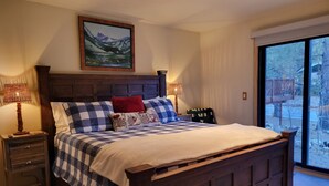 A bedroom with a large bed, two nightstands, a painting above the bed, and a view through a large window. - Four Seasons Getaway-Private Spa-Walk to Village and Pineknot Trailhead-King Bed (Big Bear Lake)