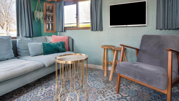 Un salon comprenant un canapé, un fauteuil gris, une table basse ronde et deux tabourets en bois.