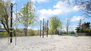 Un espacio al aire libre con arena, juegos infantiles, árboles y un banco.